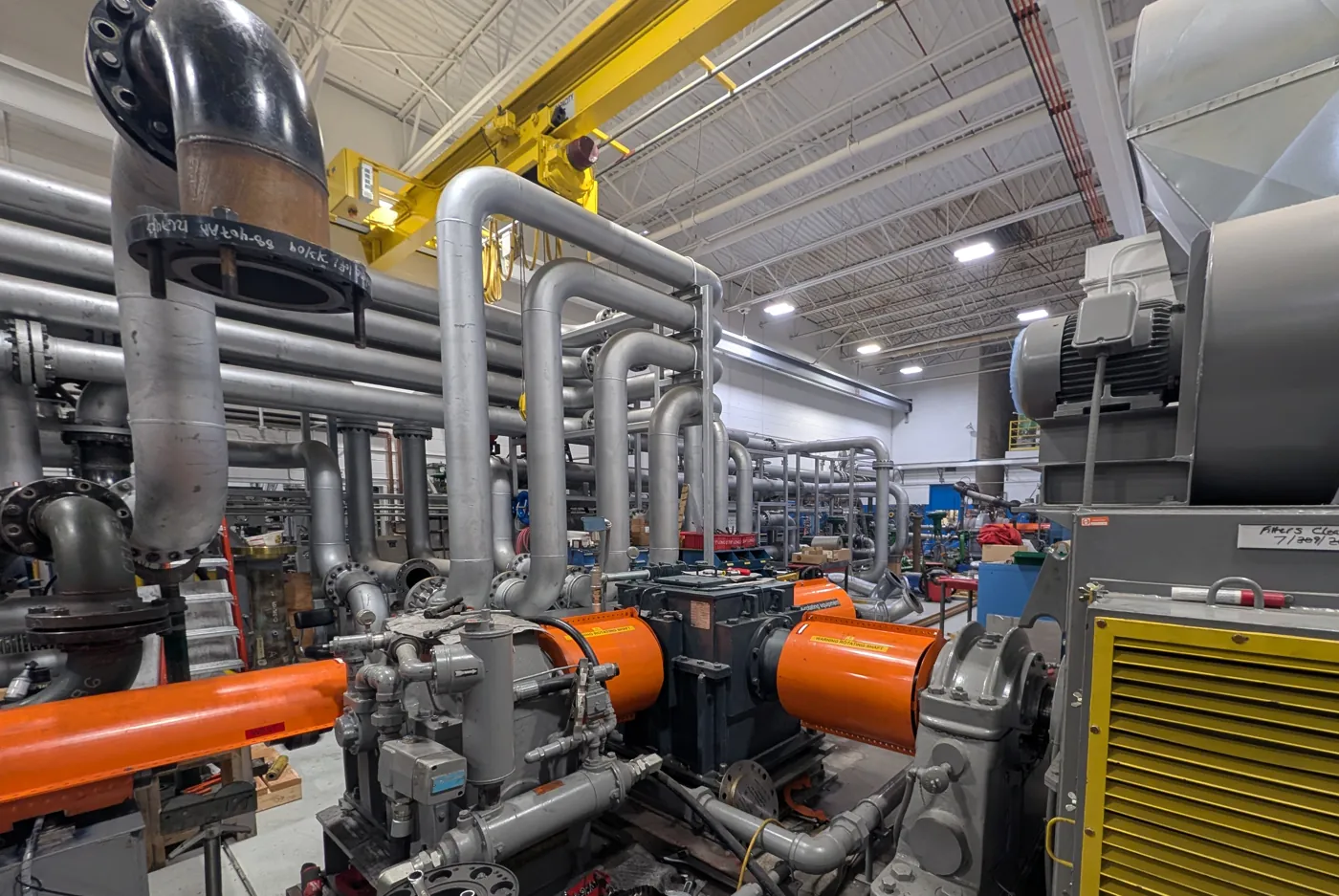 Test stand drive train with shop motor, gear unit and orange coupling guards beside the test loop piping